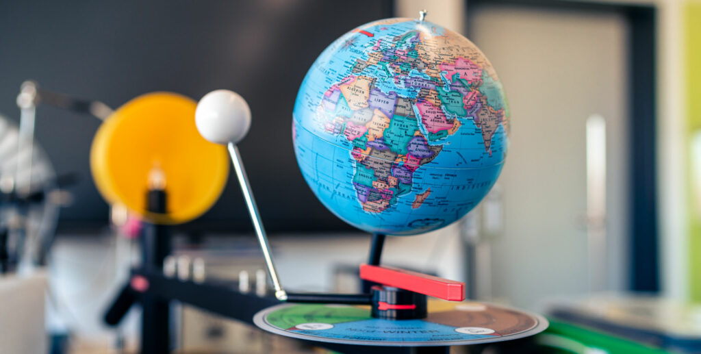 Blauer Globus mit farbiger Weltkarte, montiert auf einer Halterung mit einer gelben Scheibe.