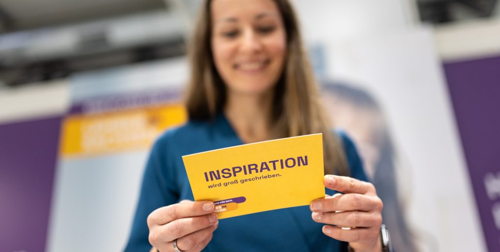 Frau hält eine gelbe Inspirationskarte mit dem Text 'INSPIRATION' in der Hand.