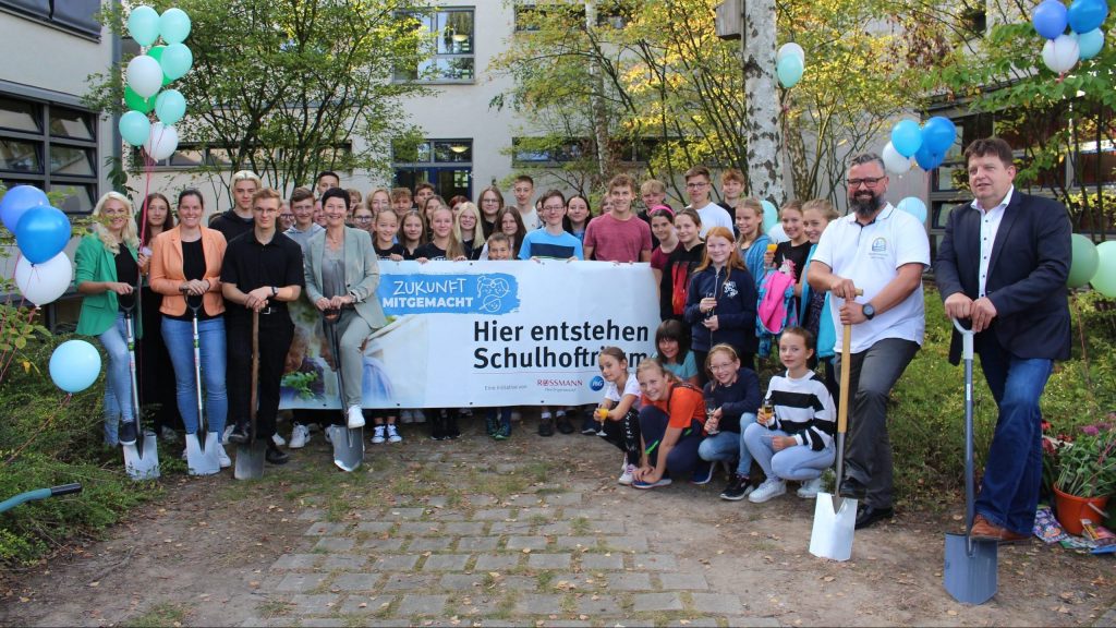 Gruppenfoto von Schülern und Erwachsenen mit Schaufeln und einem Banner für ein Schulhofprojekt.