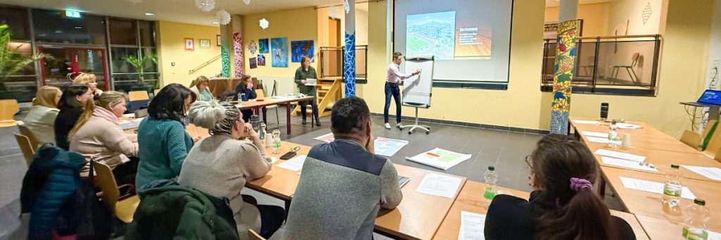 In einem Hufeisen sitzen zahlreiche Lehrer an Tischen. Im Hintergrund notiert ein Lehrer die Auszählung einer Abstimmung auf ein Flipchart.