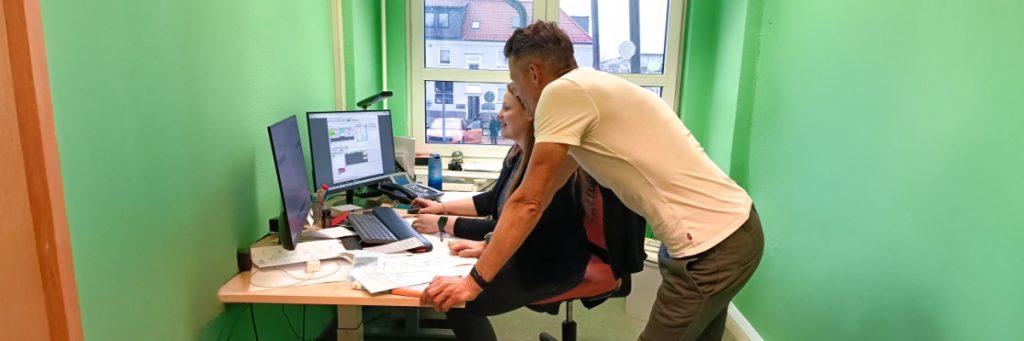 In einem grün gestrichenen Raum beugen sich Schulleiter Ronny Staudte, auf den Tisch gestützt im Vordergrund, und der stellvertretenden Schulleiterin Laura Fabian vor einem Computer an der Bruno-Bürgel-Oberschule in Weißwasser.