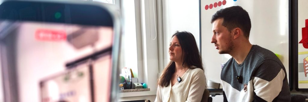 Ein Mann und eine Frau vor einer Pinwand mit roten Punkten aufgeklebt.