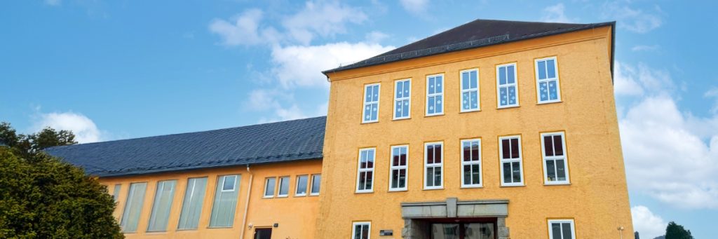 Eingangsgebäude einer Schule mit gelb verputzter Fassade.