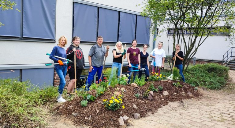 Eine Gruppe von acht Personen steht im Garten und hält Gartengeräte in der Hand.