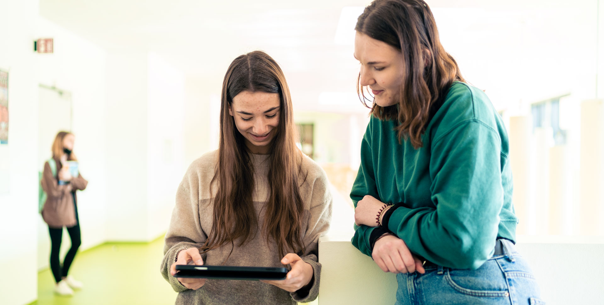 2 Schülerinnen stehen im Schulflor und schauen gemeinsam auf ein Tablet