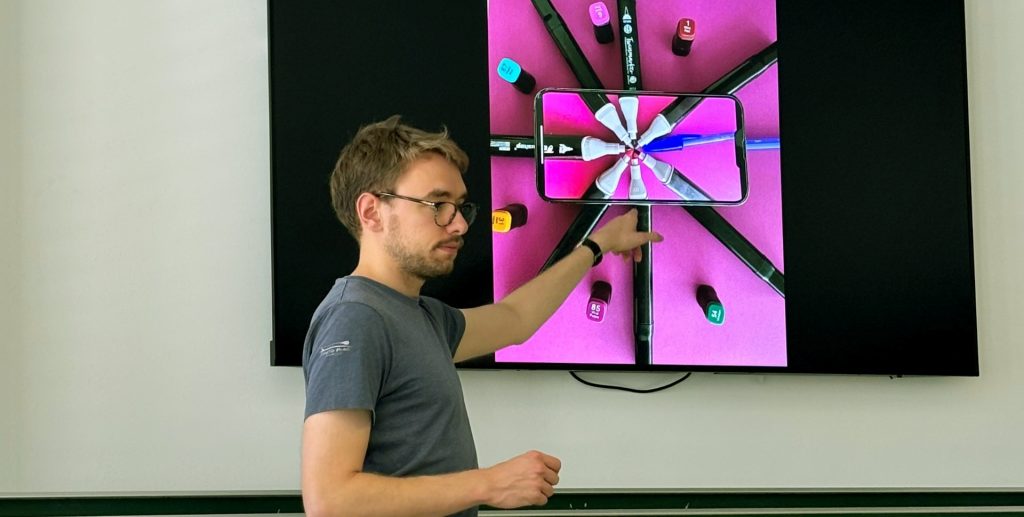 Kunstlehrer Christian Reich steht vor einem Whitboard in der Klasse und stellt ein von den Schülern erstelltes Legebild vor.