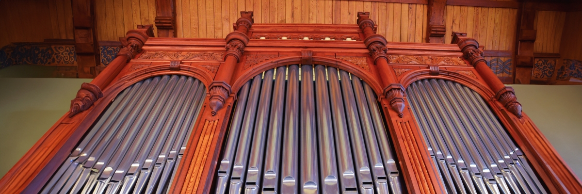 Das Bild zeigt eine Orgel aus rötlichem Holz mit silbernen Orgelpfeifen.