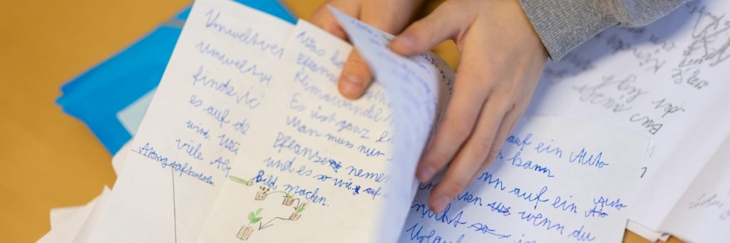 Ein Kind blättert in seinem Grundschulschreibheft handschriftlich beschriebene Seiten um.