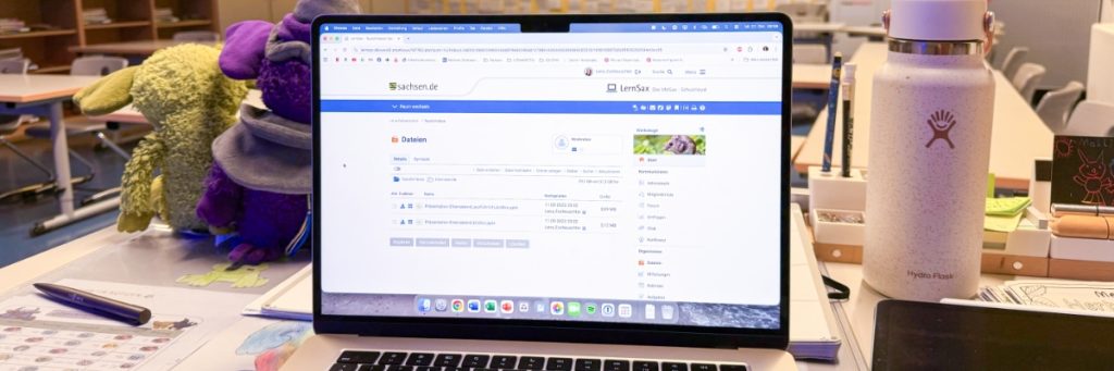 In der Mitte des Bildes ist ein aufgeklapptes Notebook mit der Website von sachsen.de und der Lernsax-Portal-Seite zu sehen.