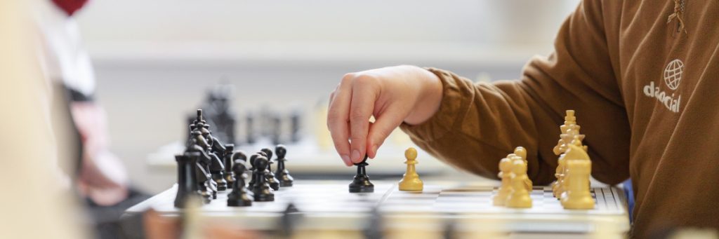 Ein Junge zieht eine Schachfigur auf dem Schachbrett. Links sind die schwarzen, rechts die weißen Figuren zu sehen, er zieht einen schwarzen Bauern.
