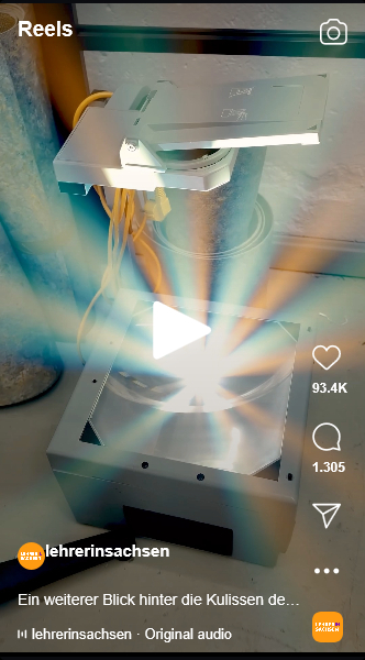 Ein technisches Gerät wirft starke bunte Lichtstrahlen in einen Innenraum, daneben stehen Reels-Elemente und lehrersachsen.