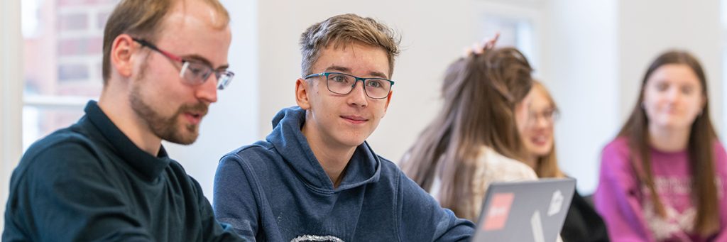 Schüler oder Studierende arbeiten bei der Herbstuniversität der TU Dresden gemeinsam an einem Laptop in einem hellen Raum