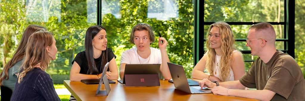Fünf Studierende der Westsächsischen Hochschule Zwickau arbeiten gemeinsam an einem Tisch in einem hellen Campusraum mit Laptops und Unterlagen.