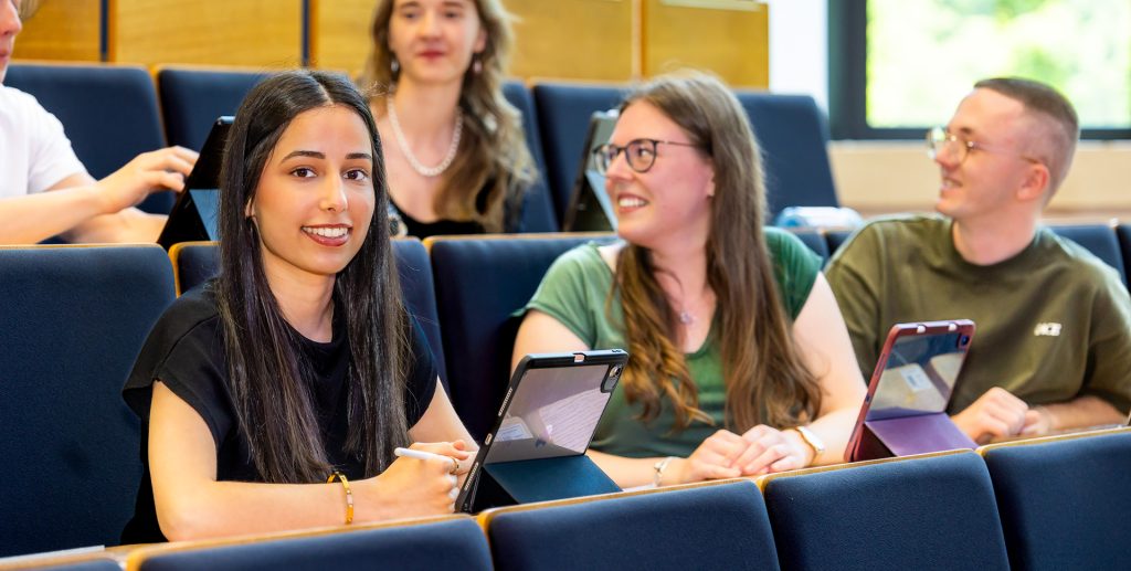 Studierende der Westsächsischen Hochschule Zwickau sitzen mit Tablets im Hörsaal und tauschen sich während einer Lehrveranstaltung angeregt aus.